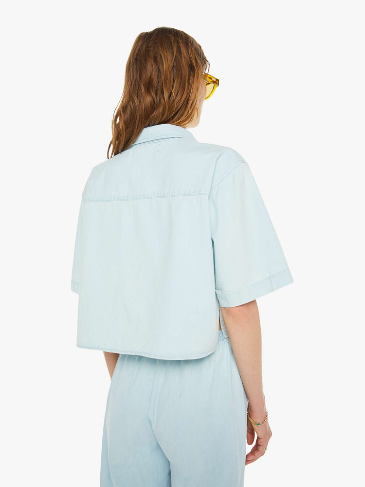  Back  view of a woman sky blue button-up blouse with a patch pocket, drop shoulders and a cropped, boxy fit.