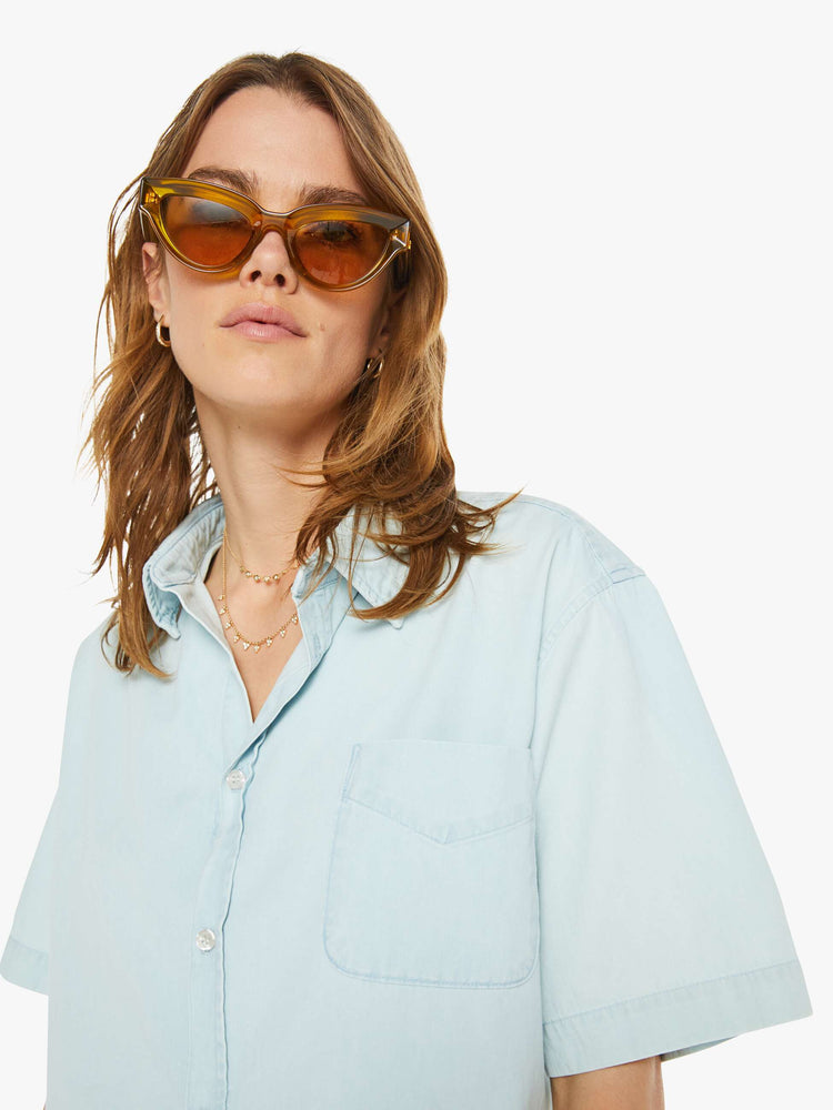 Close up  view of a woman sky blue button-up blouse with a patch pocket, drop shoulders and a cropped, boxy fit.