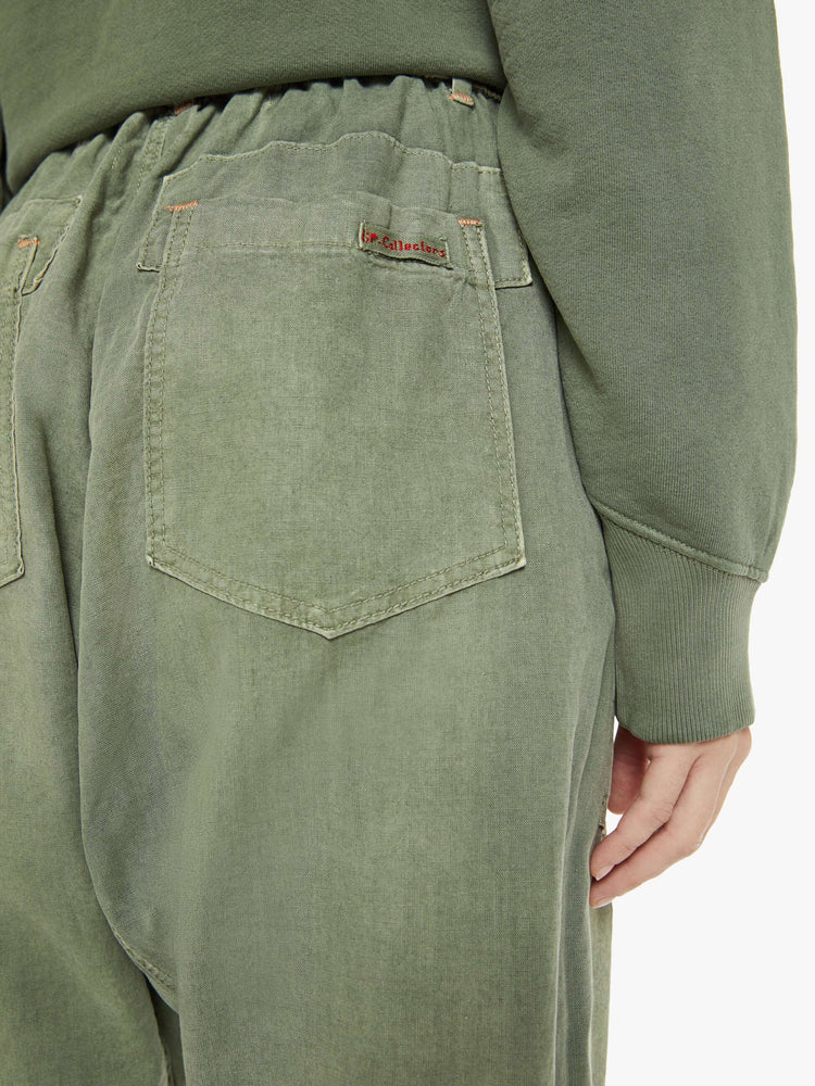 Close up view of a woman in a faded army green, the pants have a mid rise, narrow straight leg, drawstring waist with a woven belt and a loose fit.