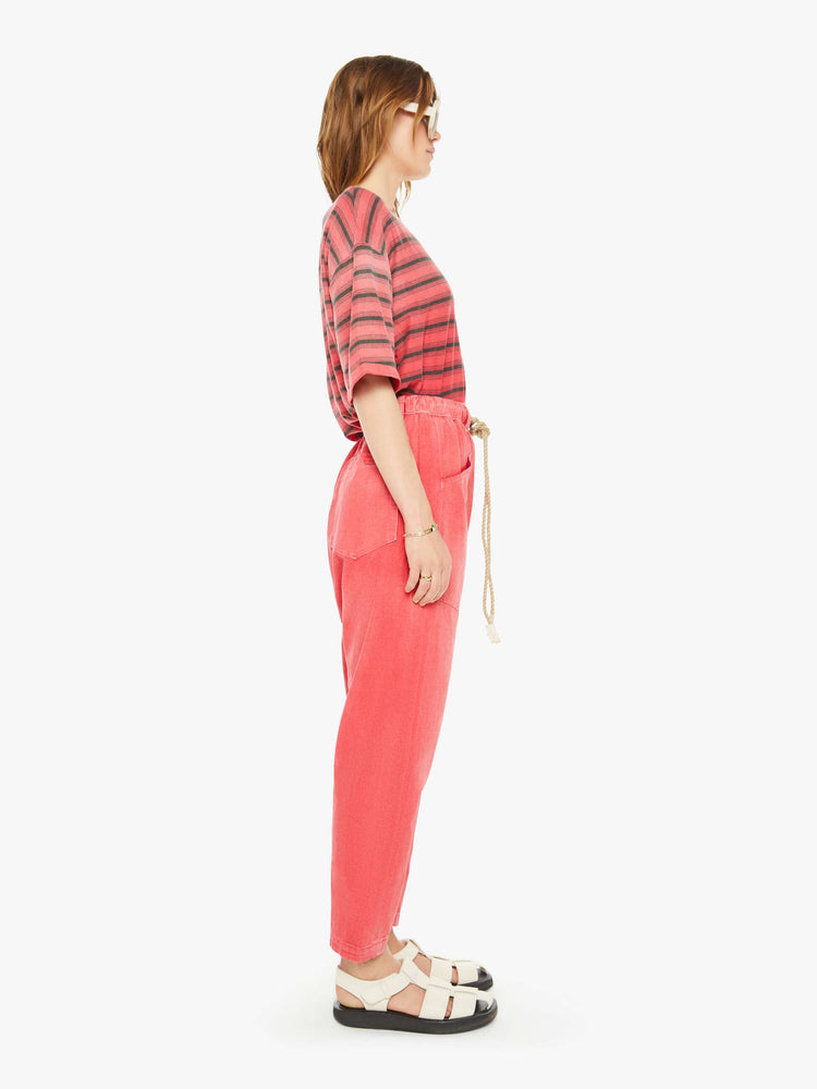 Side view of a woman red pants have a mid rise, narrow straight leg, drawstring waist with a woven belt and a loose fit.