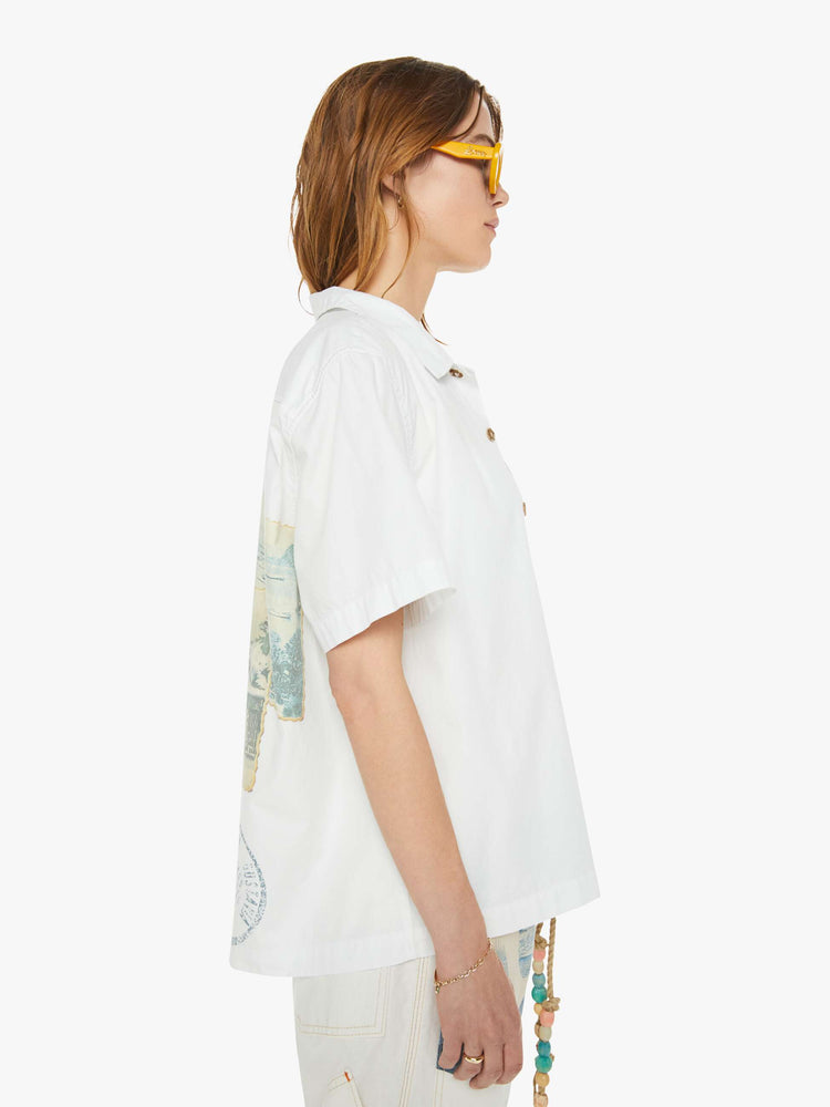 Side view of a woman in a white with blue embroidery on the chest short sleeve shirt features drop shoulders, boxy sleeves and a loose fit.