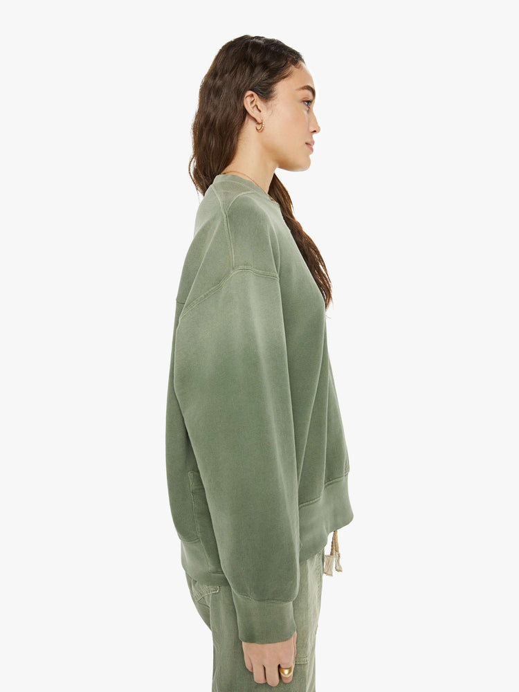 Side view of a woman in a sweatshirt that features drop shoulders, long, oversized sleeves, ribbed hems and a loose fit. It's made from 100% cotton French terry in olive green.