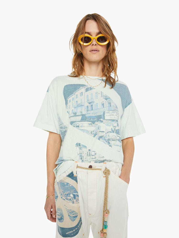 Front view of a woman drop shoulders, short sleeves and a boxy fit tee in white with a scenes from St. Tropez in faded blue.