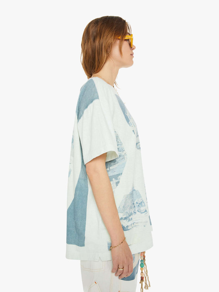 Side view of a woman drop shoulders, short sleeves and a boxy fit tee in white with a scenes from St. Tropez in faded blue.
