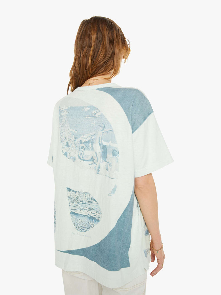 Back view of a woman drop shoulders, short sleeves and a boxy fit tee in white with a scenes from St. Tropez in faded blue.