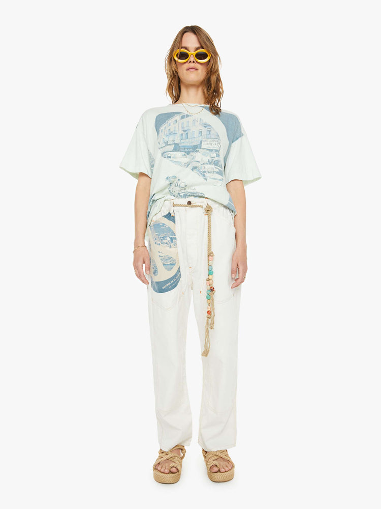 Full body view of a woman drop shoulders, short sleeves and a boxy fit tee in white with a scenes from St. Tropez in faded blue.