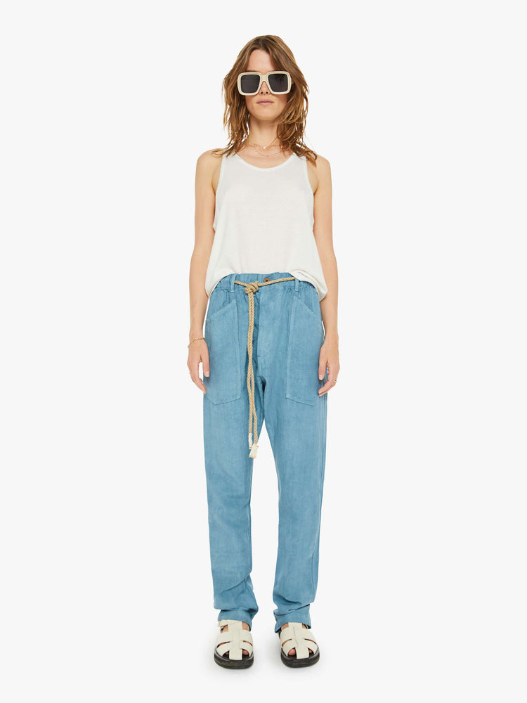 Front view of a woman teal blue pants have a mid rise, narrow straight-leg, patch pockets, drawstring waist with a woven belt and a loose fit.