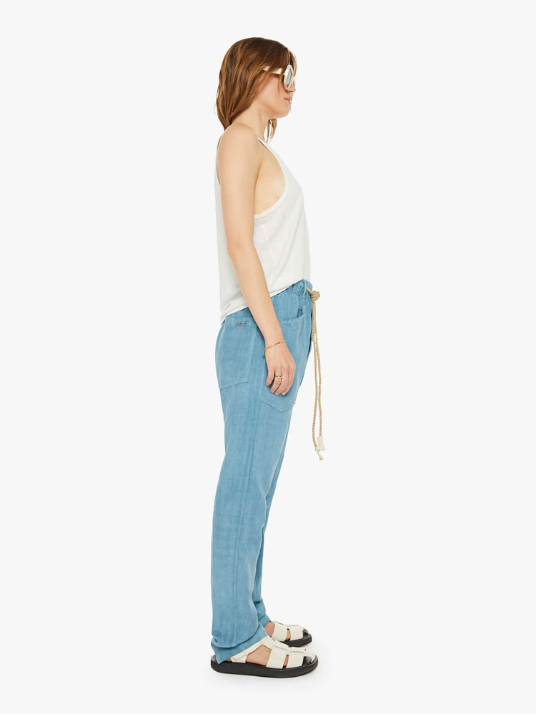 Side view of a woman teal blue pants have a mid rise, narrow straight-leg, patch pockets, drawstring waist with a woven belt and a loose fit.