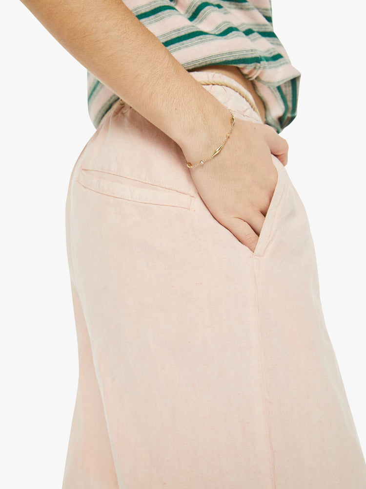 Close up view of a woman in a rose pink pant with a mid rise, flared leg, patch pockets and pleats at the waist for a loose fit.