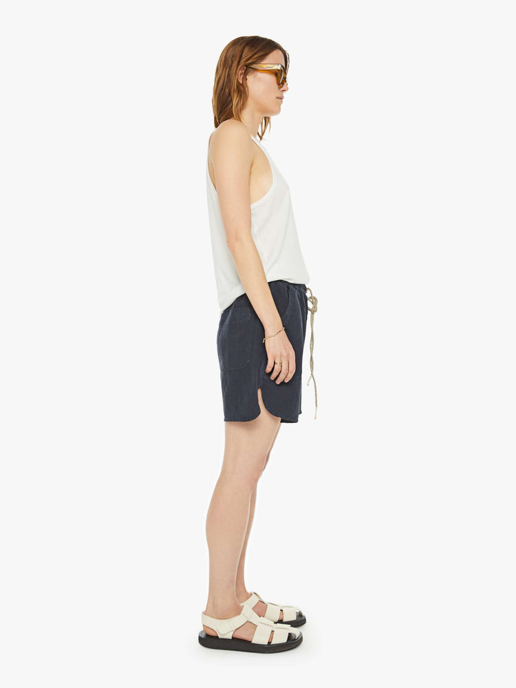 Side view of a woman in a black short with mid rise, drawstring elastic waist, deep patch pockets, a loose fit and a long inseam that hits just above the knee.