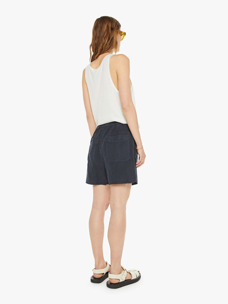 Back view of a woman in a black short with mid rise, drawstring elastic waist, deep patch pockets, a loose fit and a long inseam that hits just above the knee.