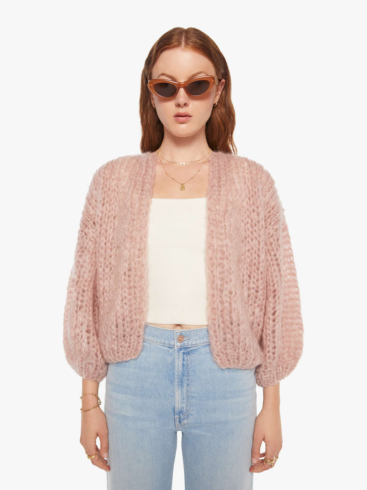 Front view of a woman in a hand knit baby pink cardigan with drop shoulders  and bracelet-length balloon sleeves. 