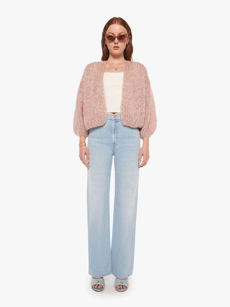 Full body view of a woman in a hand knit baby pink cardigan with drop shoulders  and bracelet-length balloon sleeves. 