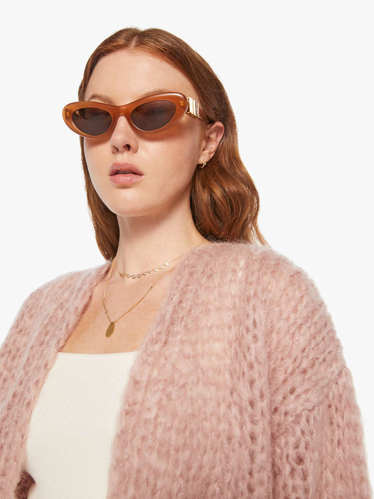 Close up view of a woman in a hand knit baby pink cardigan with drop shoulders  and bracelet-length balloon sleeves. 