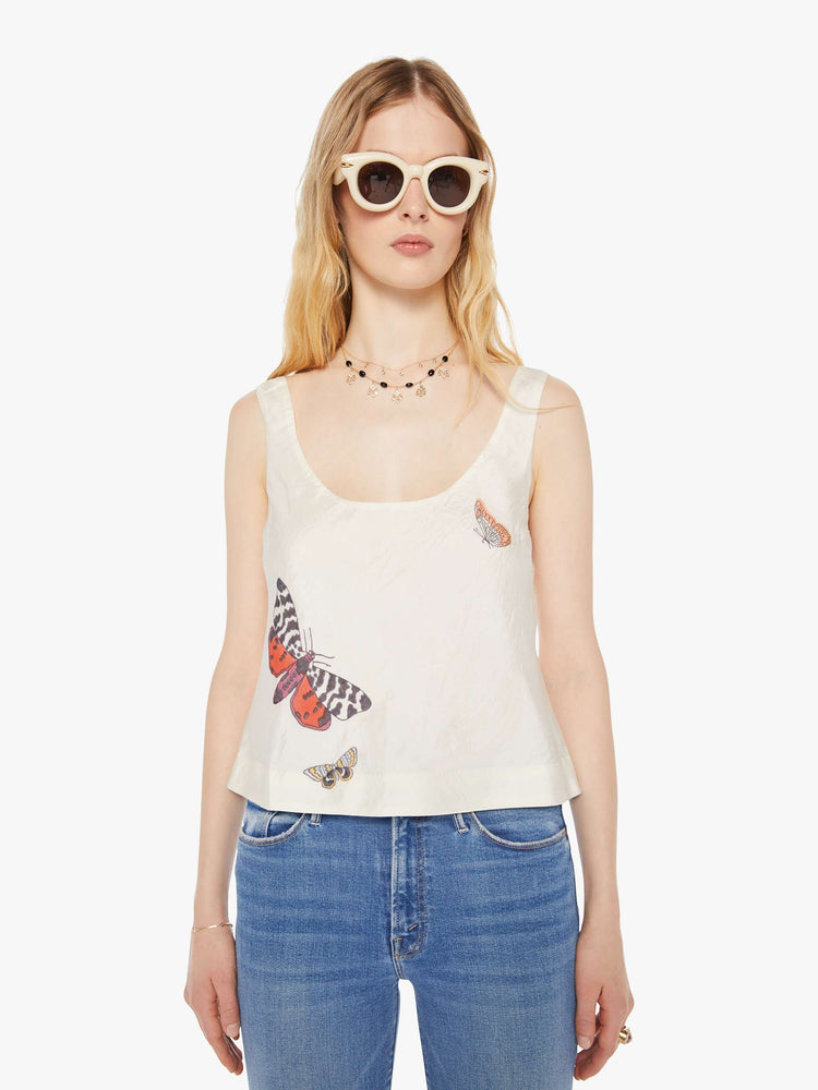 Front view of a woman in a cream sleeveless top with embroidered butterflies on the front, and features a deep scoop neck and a cropped, boxy fit.