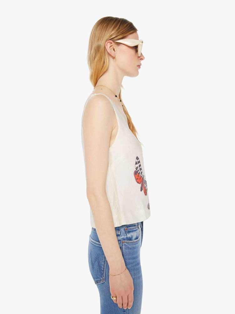 Side view of a woman in a cream sleeveless top with embroidered butterflies on the front, and features a deep scoop neck and a cropped, boxy fit.