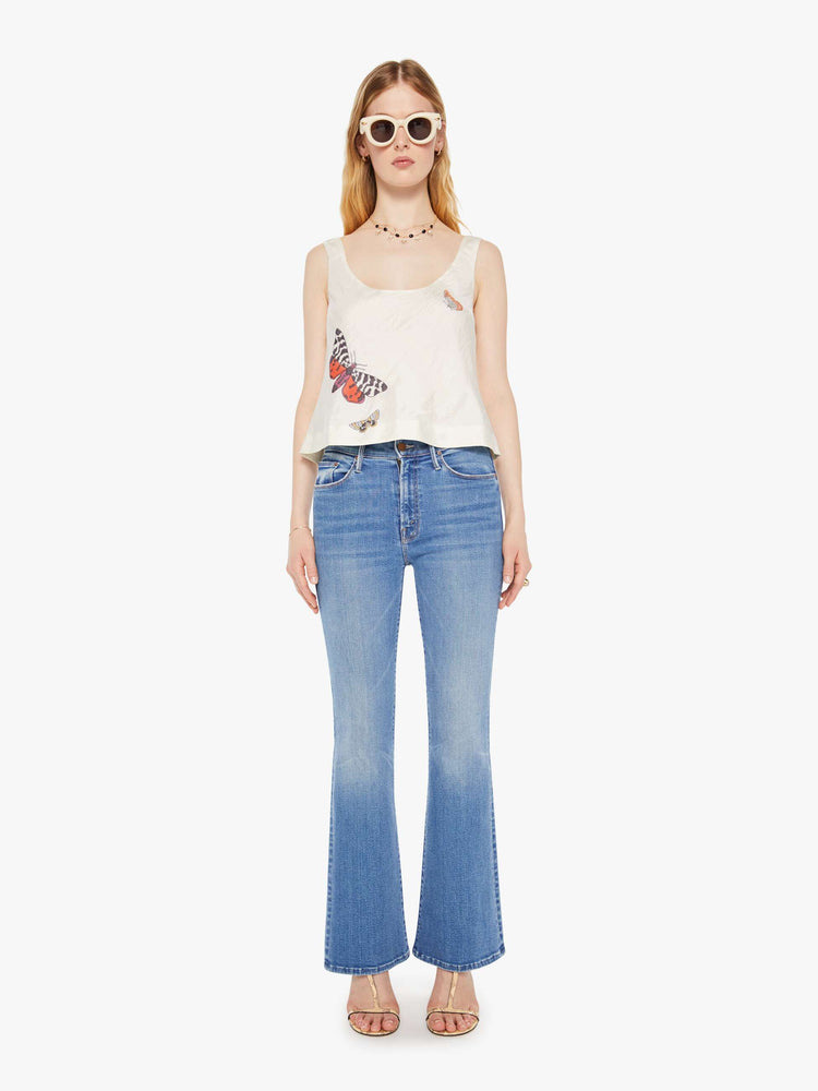 Full body view of a woman in a cream sleeveless top with embroidered butterflies on the front, and features a deep scoop neck and a cropped, boxy fit.