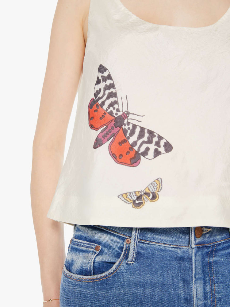 Close up view of a woman in a cream sleeveless top with embroidered butterflies on the front, and features a deep scoop neck and a cropped, boxy fit.