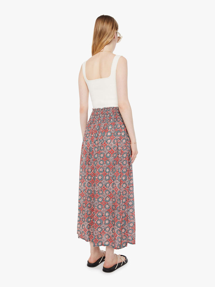 Back view of a woman in a skirt with  a terracotta and blue graphic print inspired by Spanish tiles and has a smocked waistband and a loose, flowy fit. 