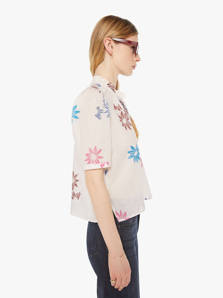Side view of a woman in a cream with a graphic floral print button down shirt with a stacked collar, puffed shoulders, elbow-length sleeves.