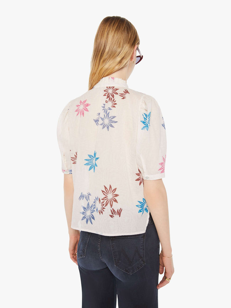 Back view of a woman in a cream with a graphic floral print button down shirt with a stacked collar, puffed shoulders, elbow-length sleeves.
