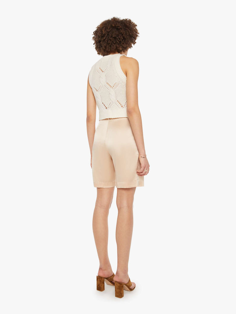 Back view of a woman in a neutral pink high-waisted short with a pleated waistband, side slit pockets and a loose straight leg.