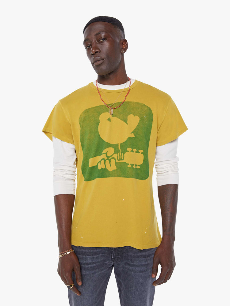 MEN front view in a  mustard yellow tee that pays homage to the legendary Woodstock festival with a green graphic on the front.