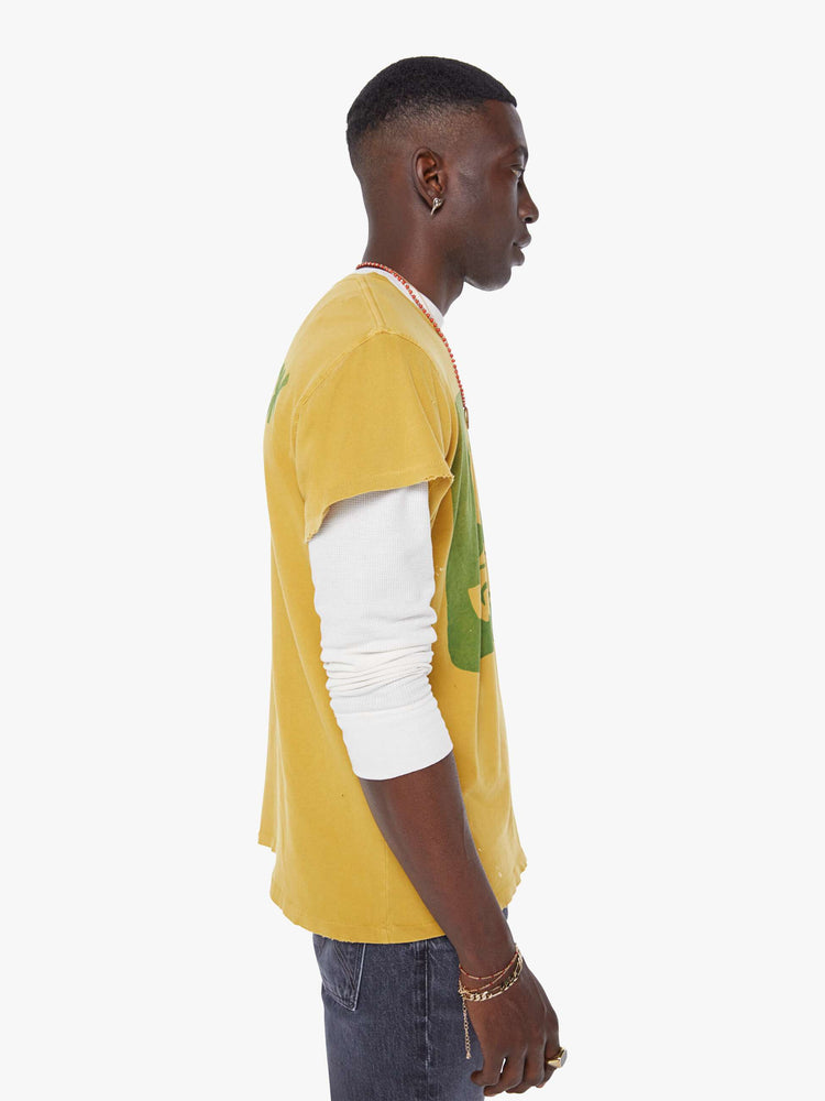MEN side view in a  mustard yellow tee that pays homage to the legendary Woodstock festival with a green graphic on the front.