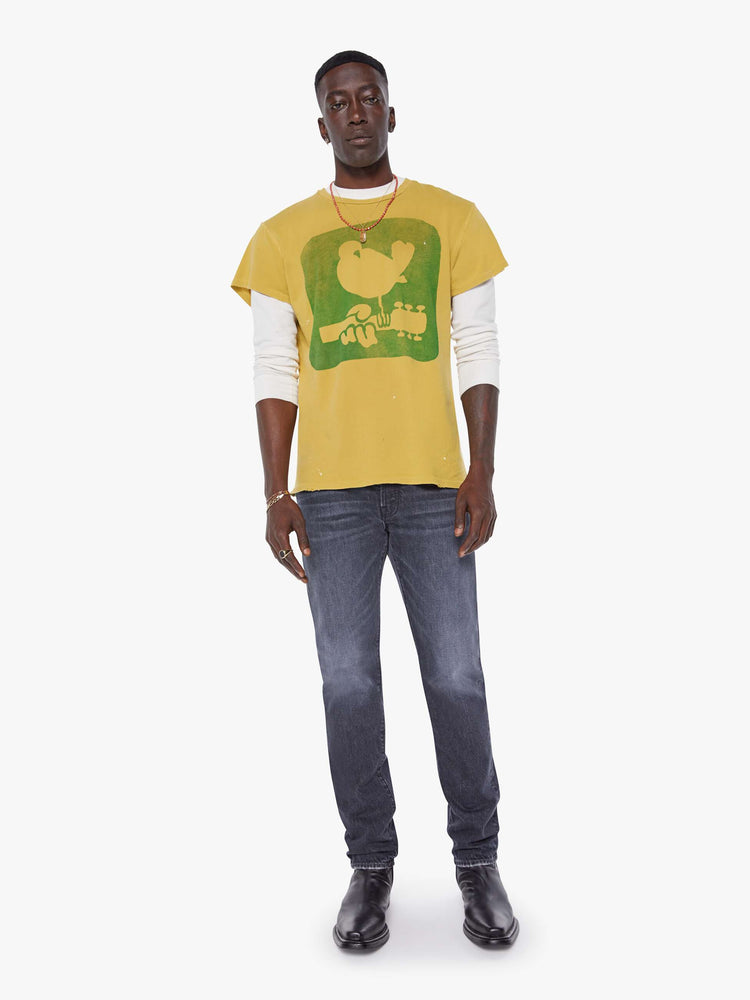 MEN full body view in a  mustard yellow tee that pays homage to the legendary Woodstock festival with a green graphic on the front.