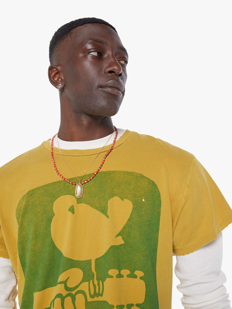 MEN close up view in a  mustard yellow tee that pays homage to the legendary Woodstock festival with a green graphic on the front.