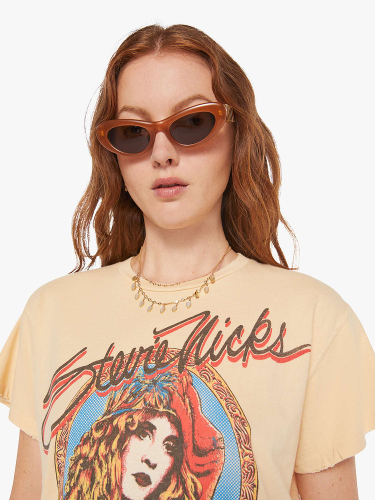 Close up view of a woman in a light yellow, the tee pays homage to Stevie Nicks' Rock A Little tour with a graphic portrait on the front.