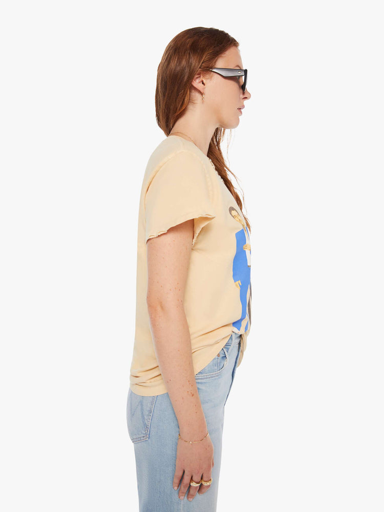 Side view of a woman in a light yellow tee that pays homage to the B-52s with a graphic portrait on the front.