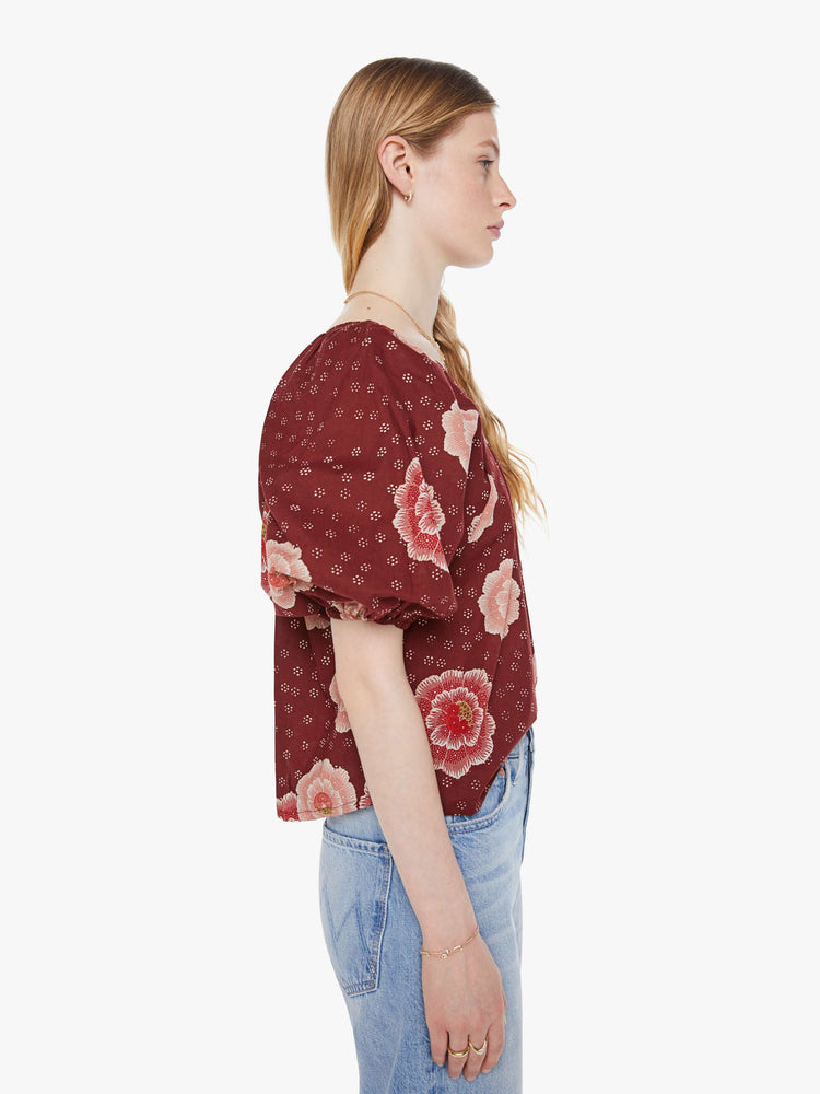 Side view of a woman in a maroon with a pink poppy print shirt with elastic boat neck that can be worn off-the-shoulder, 3/4-length balloon sleeves and a flowy fit.