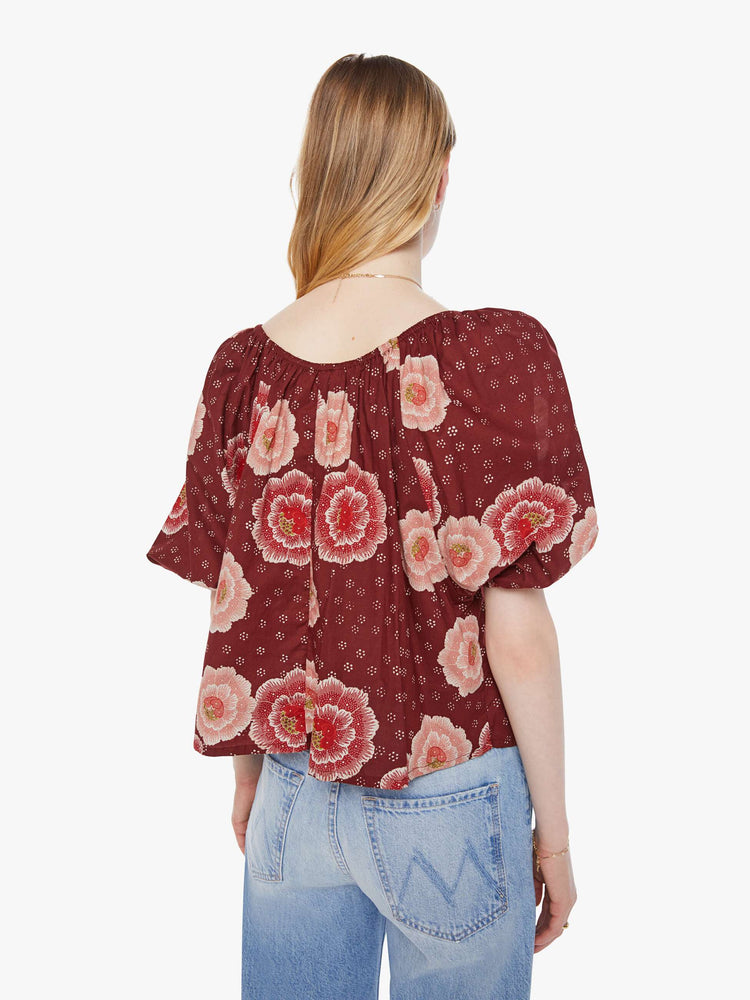 Back view of a woman in a maroon with a pink poppy print shirt with elastic boat neck that can be worn off-the-shoulder, 3/4-length balloon sleeves and a flowy fit.