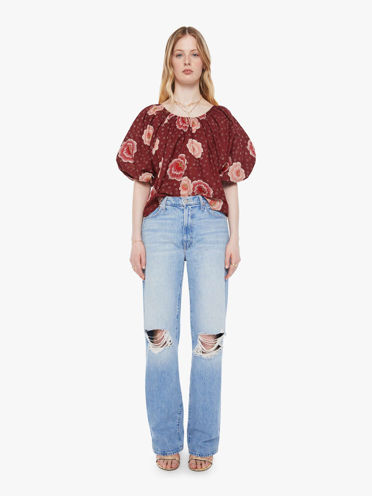 Full view of a woman in a maroon with a pink poppy print shirt with elastic boat neck that can be worn off-the-shoulder, 3/4-length balloon sleeves and a flowy fit.