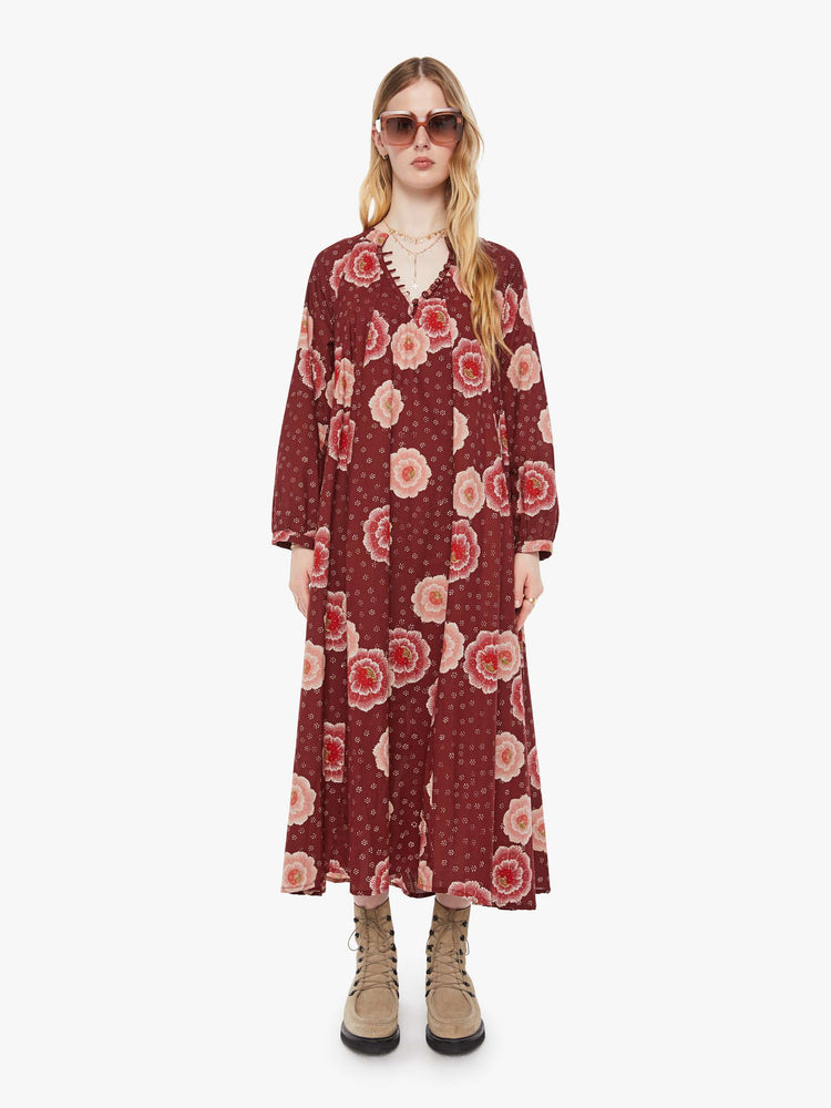 Front view of a woman in a  maroon with a pink poppy print, this maxi dress is designed with voluminous sleeves and has an A-line cut for a loose, breezy feel.