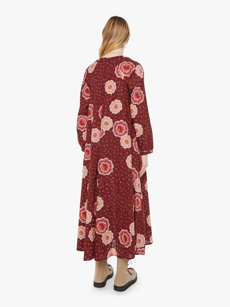 Back view of a woman in a  maroon with a pink poppy print, this maxi dress is designed with voluminous sleeves and has an A-line cut for a loose, breezy feel.
