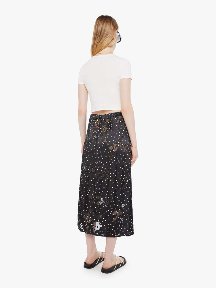 Back view of a woman in a black with white polka dots, the skirt has a high rise, calf-length hem and a loose, flowy fit.