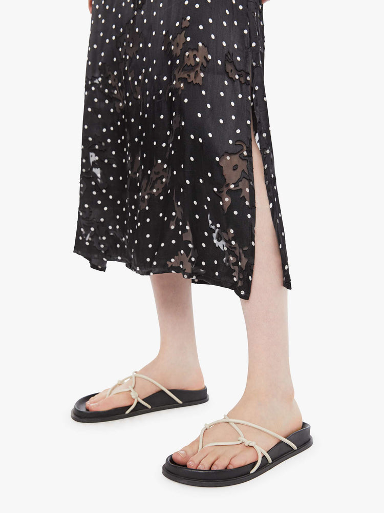 Hem view of a woman in a black with white polka dots, the skirt has a high rise, calf-length hem and a loose, flowy fit.