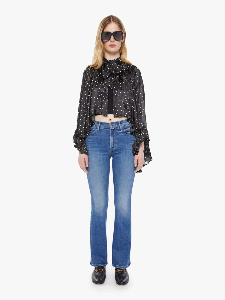 Full body view of a woman in a black with white polka dots cape with a tied V-neck, open front, long billowy sleeves with ruffles at the wrists and a cropped hem.