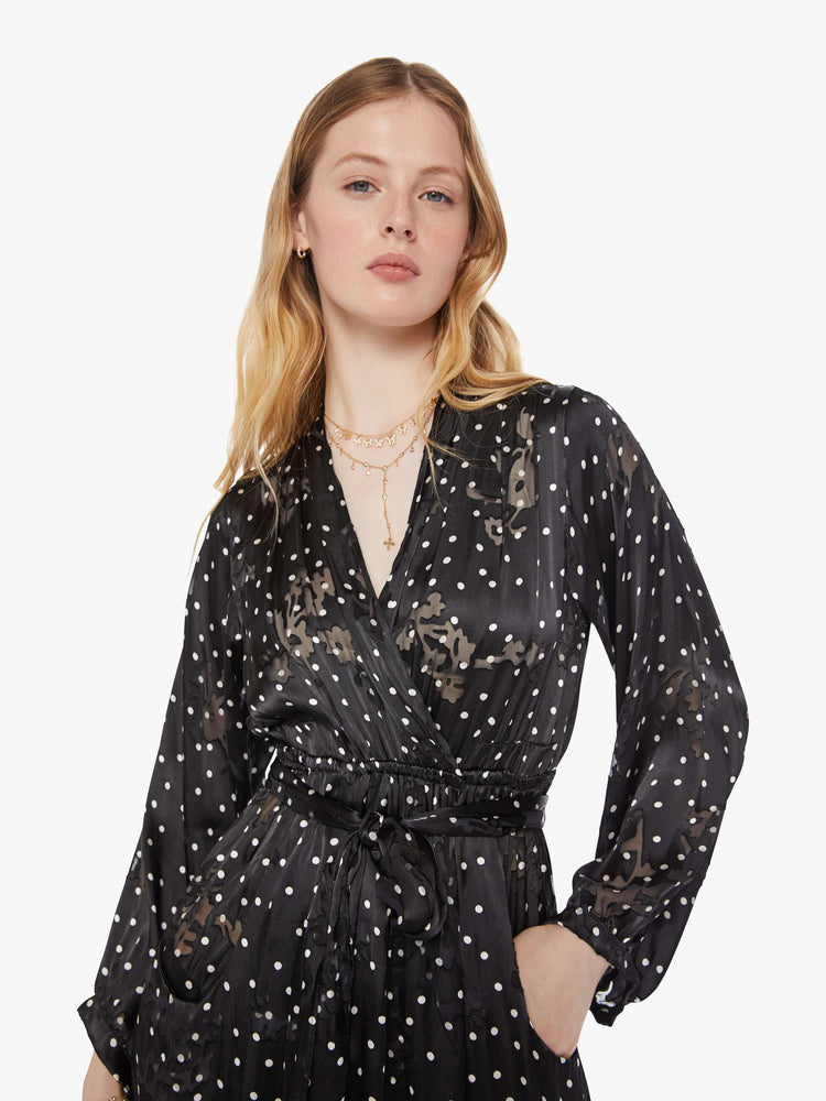 Close up view of a woman in a black and white polka dot maxi dress features a V-neck, elastic waist, two front pockets and comes with a removable sash belt.