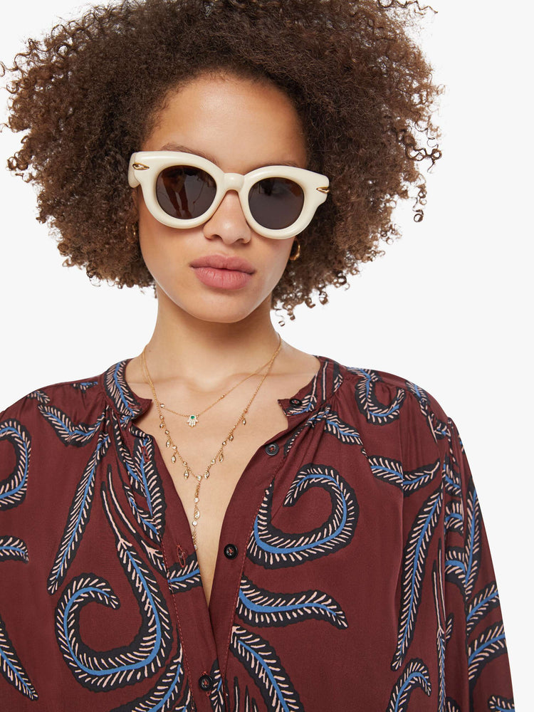 Close up view of a woman in oversized blue feather print top with a band collar, long balloon sleeves and is slightly pleated at the shoulders for a flowy fit.