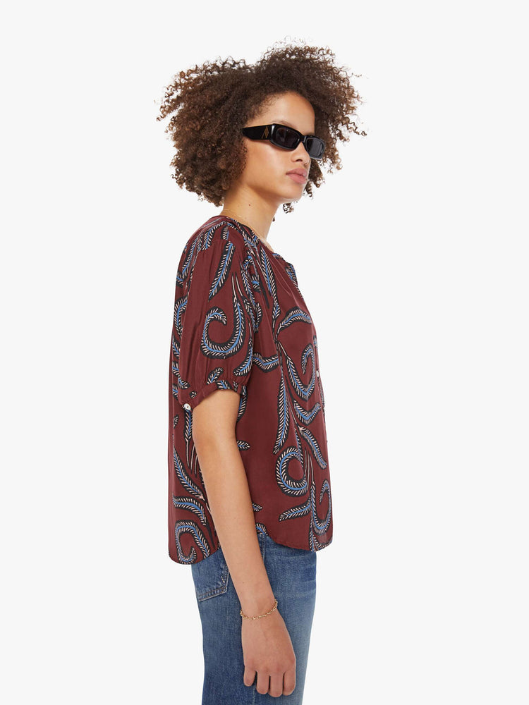 Side view of a woman in top is designed with a deep V-neck, buttons down the front, short sleeves and is slightly pleated under the collar for a loose, flowy fit.