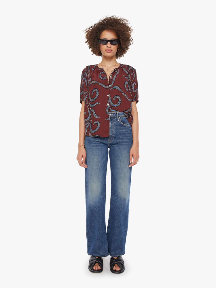 Full body view of a woman in top is designed with a deep V-neck, buttons down the front, short sleeves and is slightly pleated under the collar for a loose, flowy fit.