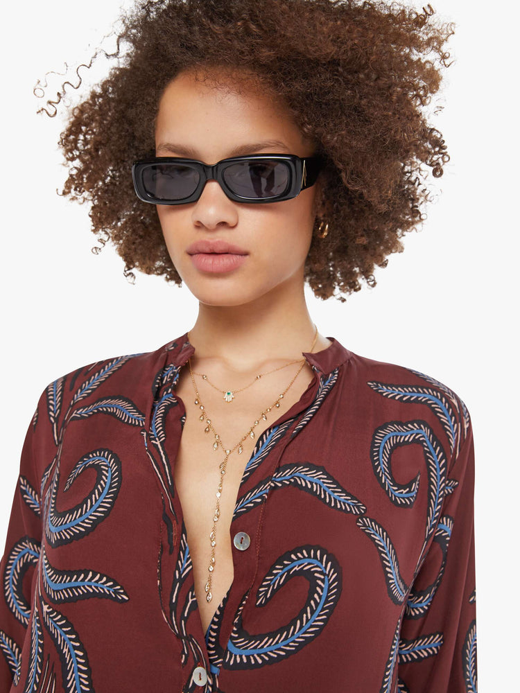 Close up view of a woman in  a flowy dress is designed with a V-neck, buttons down the front, slightly cropped long sleeves and a loose, flowy fit.