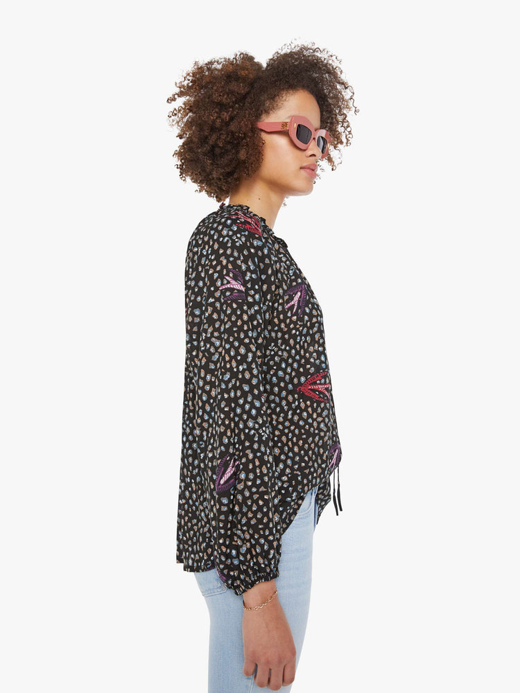 Side view of a woman in a black and white polka dot top has a keyhole neckline with a tasseled tie closure, long balloon sleeves and pleats for a loose fit.