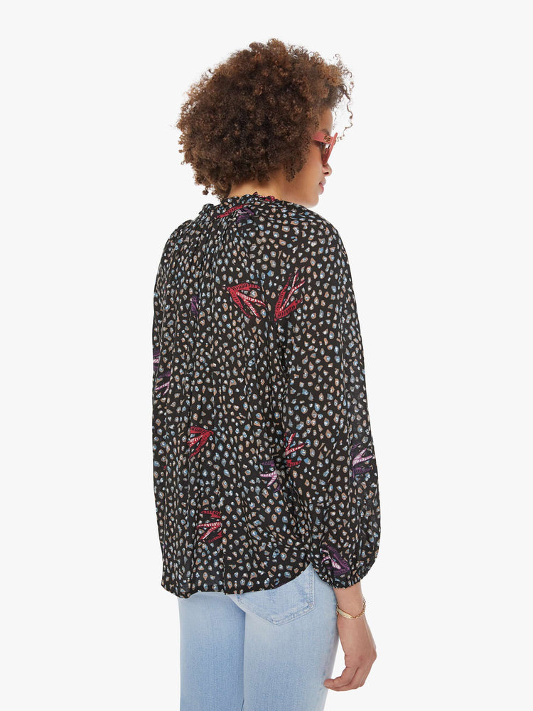 Back view of a woman in a black and white polka dot top has a keyhole neckline with a tasseled tie closure, long balloon sleeves and pleats for a loose fit.