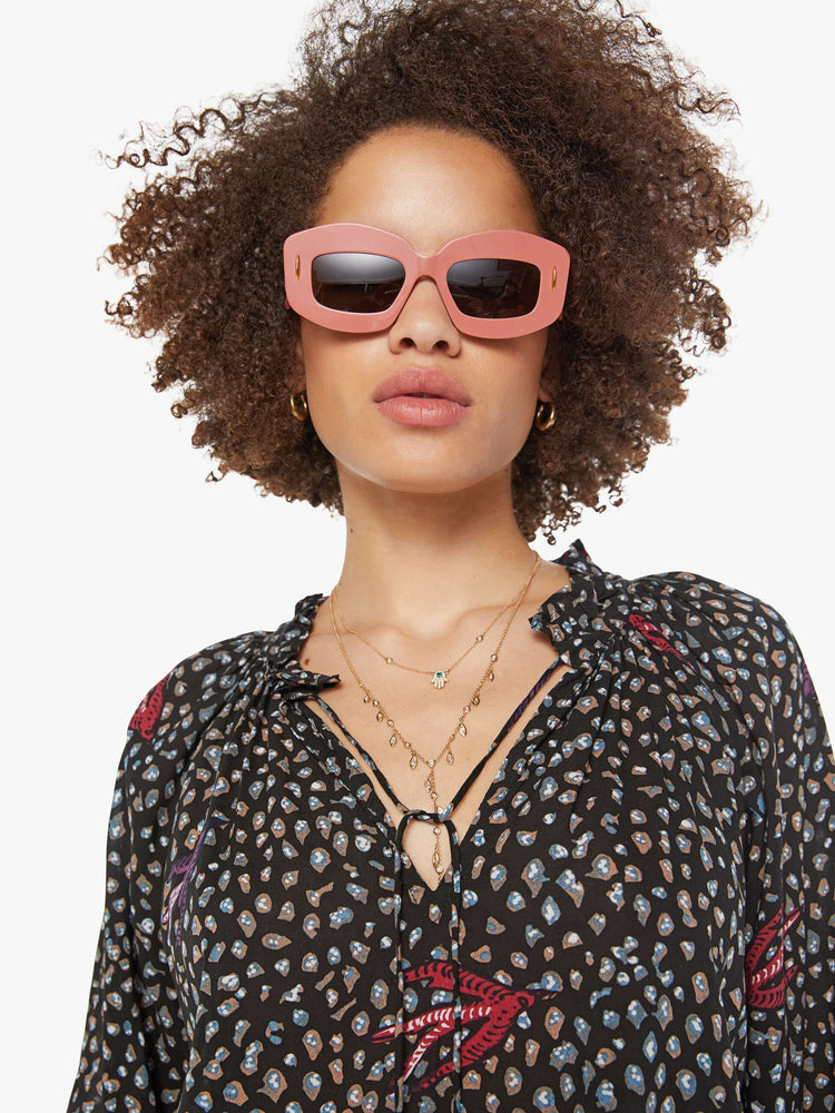 Close up view of a woman in a black and white polka dot top has a keyhole neckline with a tasseled tie closure, long balloon sleeves and pleats for a loose fit.