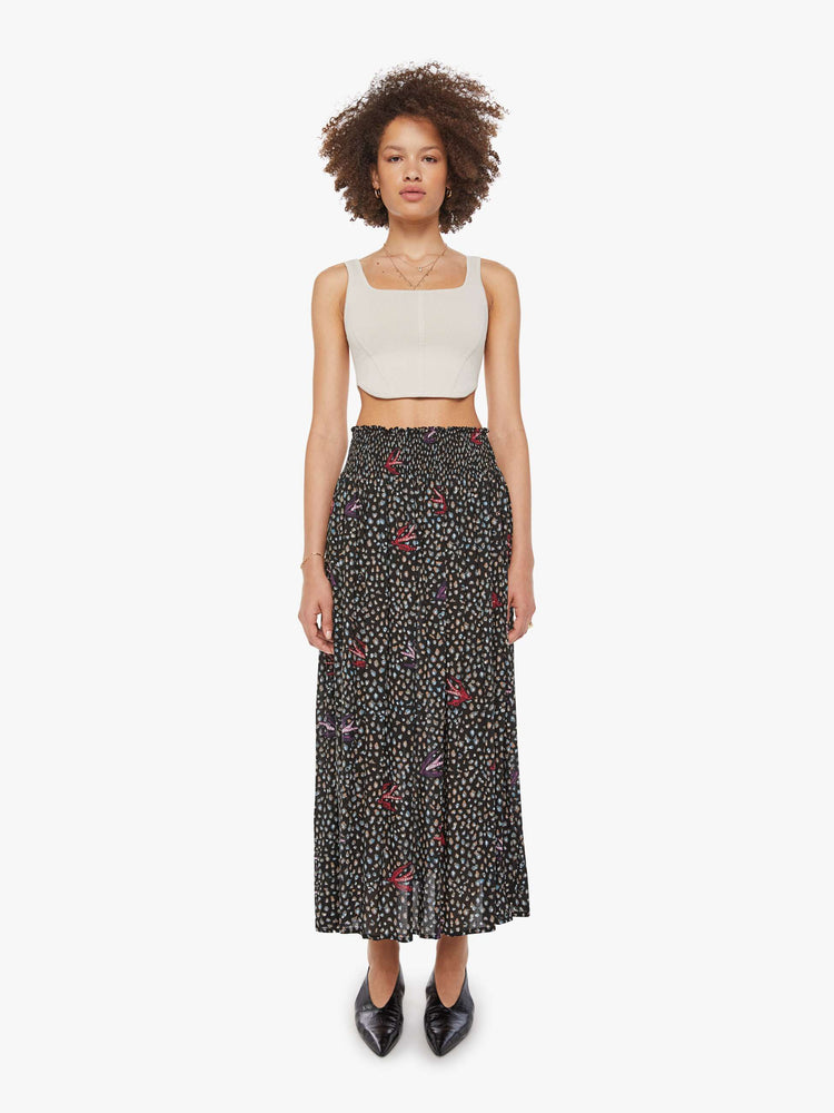 Front view of a woman in a black with white polka dots and red swallows throughout, the skirt has a smocked waistband and a loose, flowy fit.