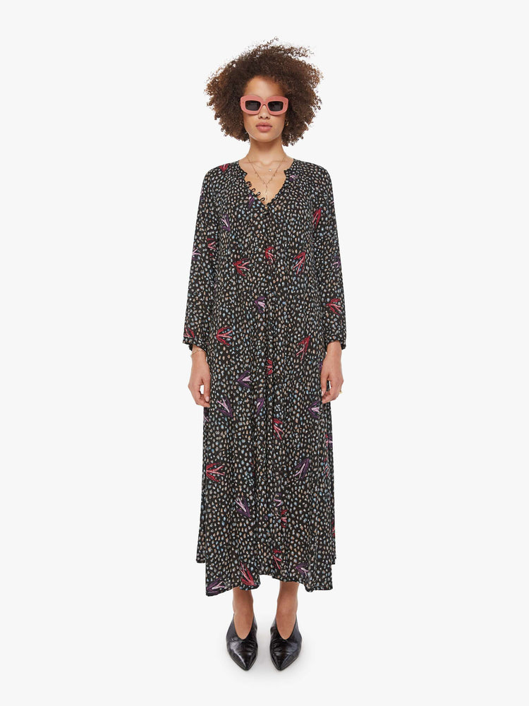 Front view of a woman in a black with white polka dots and red swallows throughout, this maxi dress has an A-line cut for a loose, breezy feel.